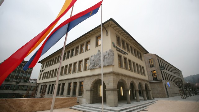 A picture of the The Liechtensteinische Landesbank in Vaduz, Liechtenstein, with twin flags blowing in the foreground.
