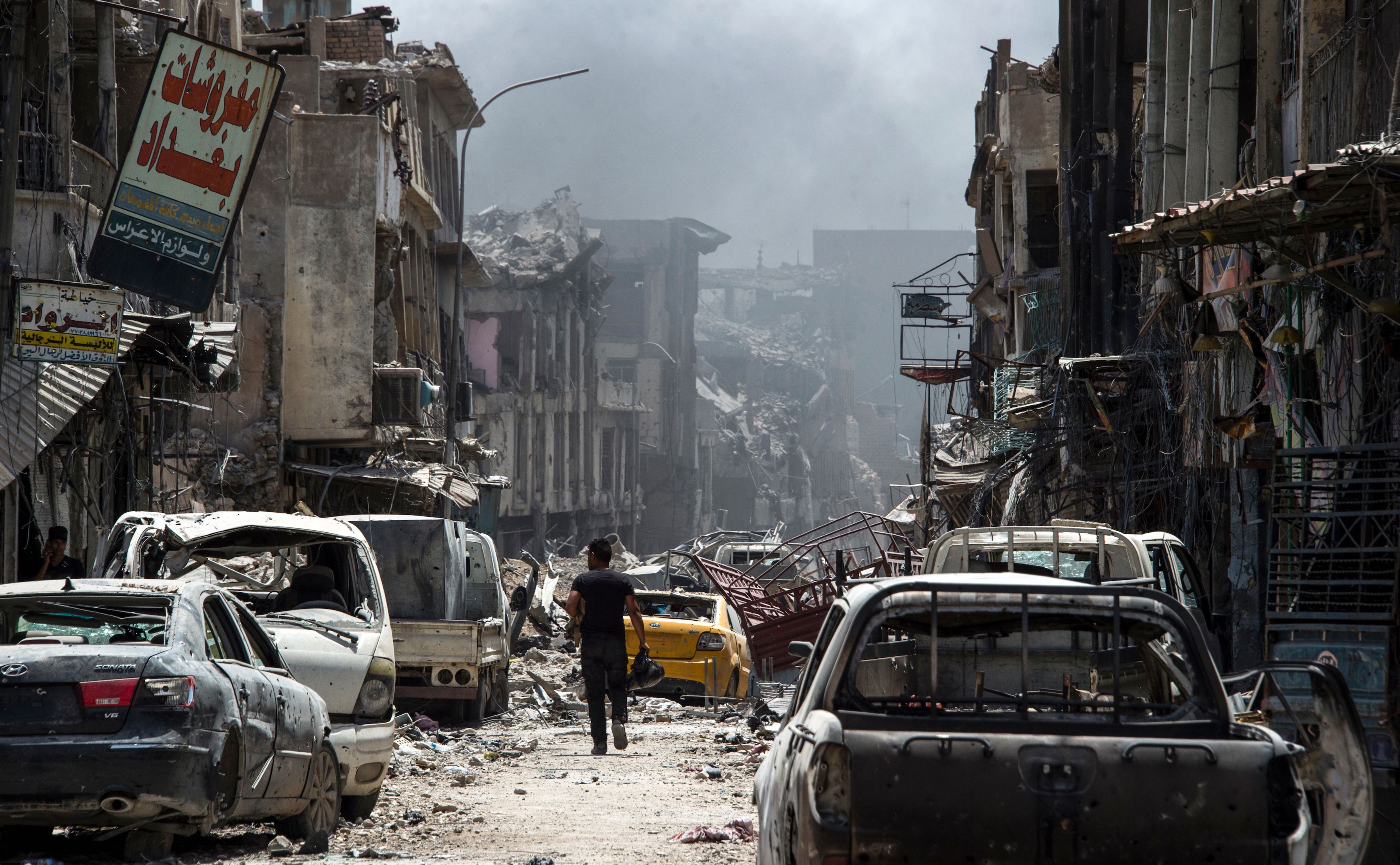 A man walks by destroyed vehicles in the Old City of Mosul, July 2. 