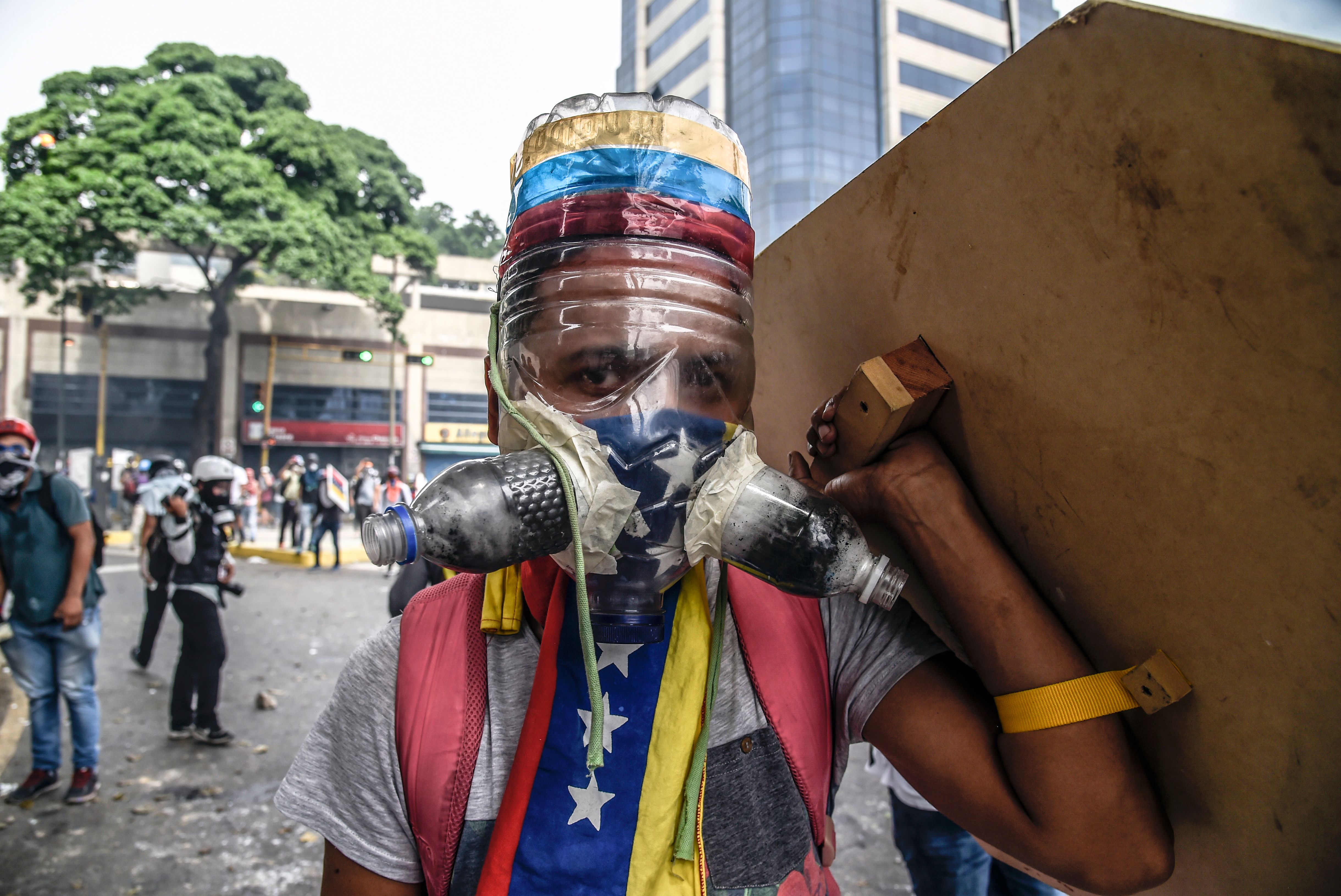 An opposition activist wearing a homemade gas mask takes cover behind a makeshift shield in Caracas on May 8. 