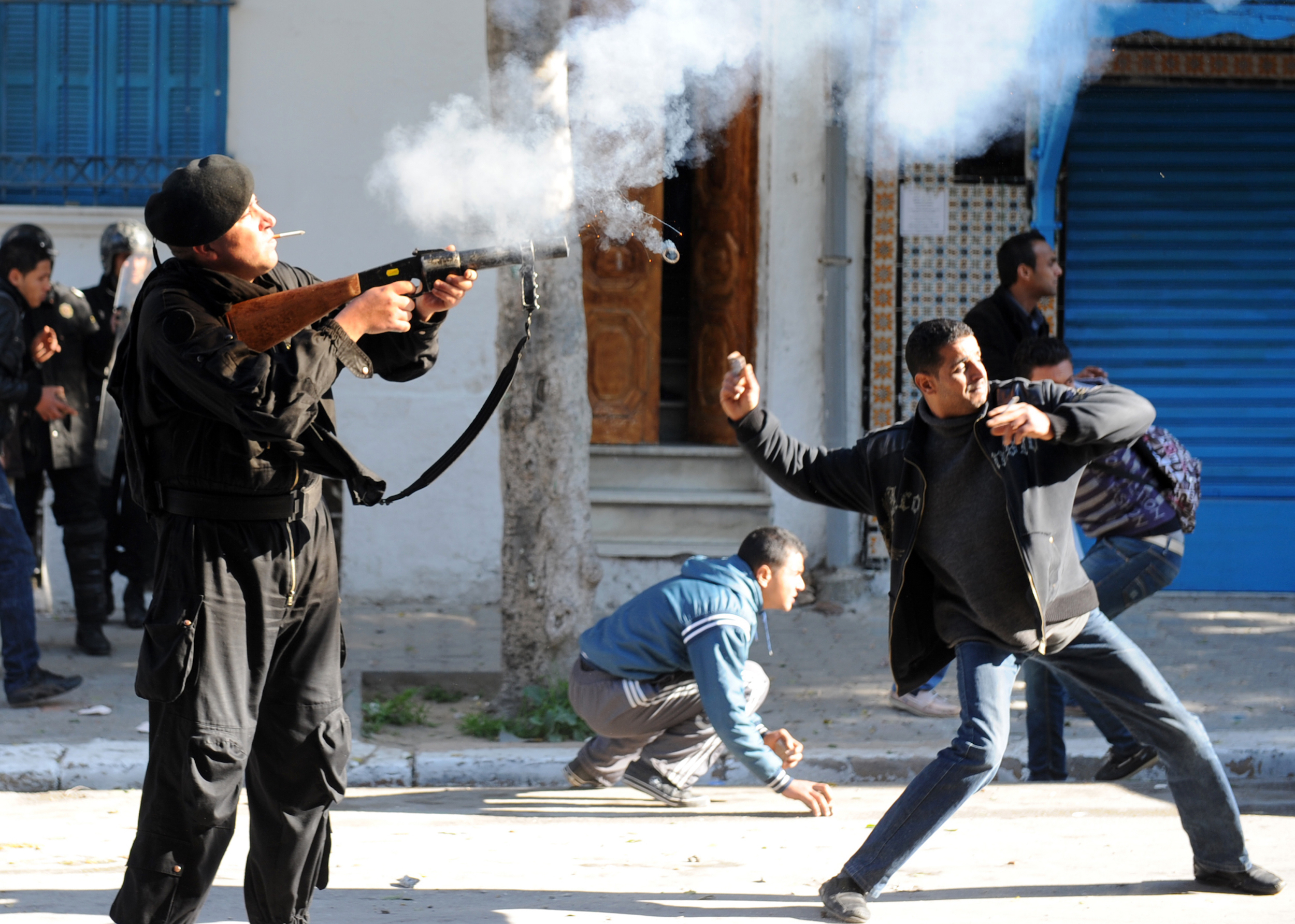 A Tunis resident throws a stone while a police officer shoots a tear gas canister on Jan. 26, 2011 in front of former Prime Minister Mohammed Ghannouchi's office.