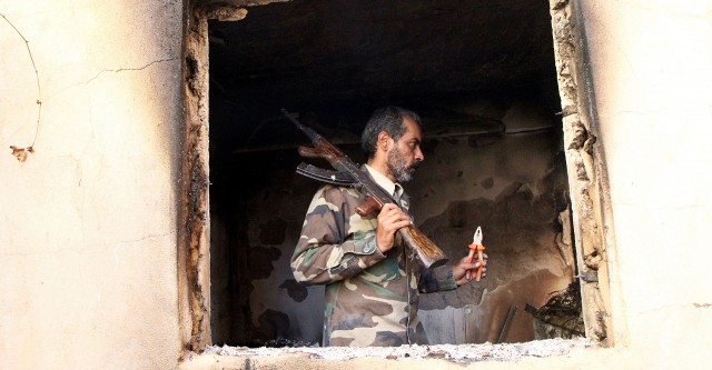 A militant fighting for Libya's Tobruk-based government searches a damaged house in Benghazi.