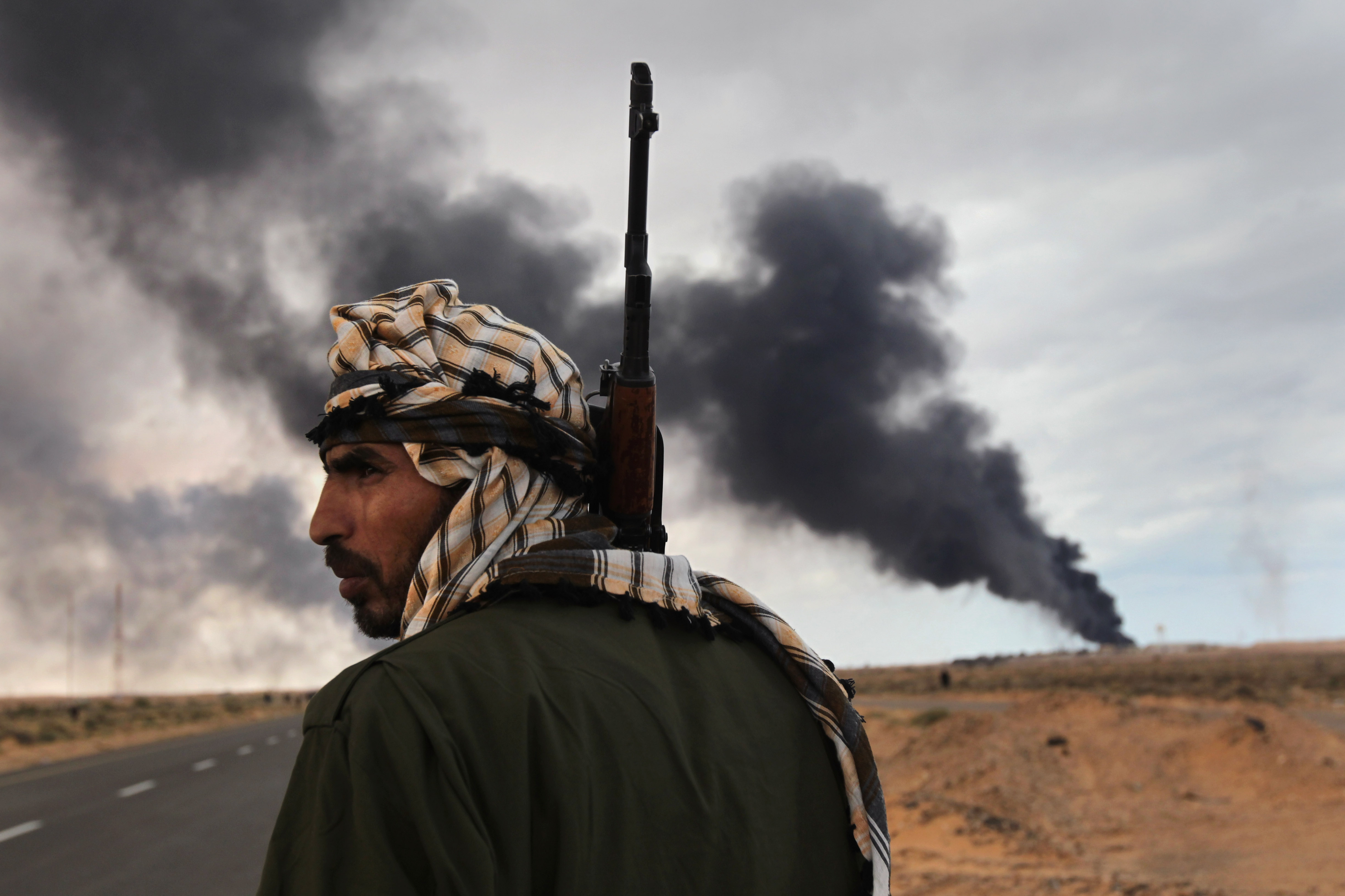 A Libyan rebel scans the frontline as a facility burns near Ras Lanuf, Libya on March 9, 2011, less than a month after anti-government protests began on Feb. 15.
