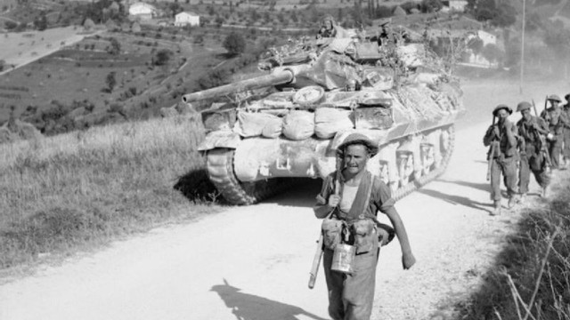 A pictures shows British troops from the 93rd Anti-Tank Regiment passing infantry of the 5th Sherwood Foresters during the advance to the Gothic Line in August 1944. 