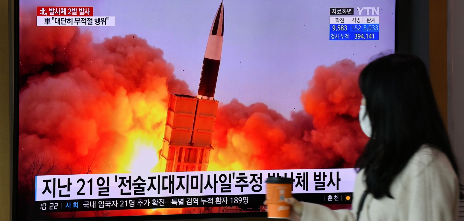 A woman walks past a screen showing footage of a North Korean missile test in Seoul, South Korea, on March 29, 2020.