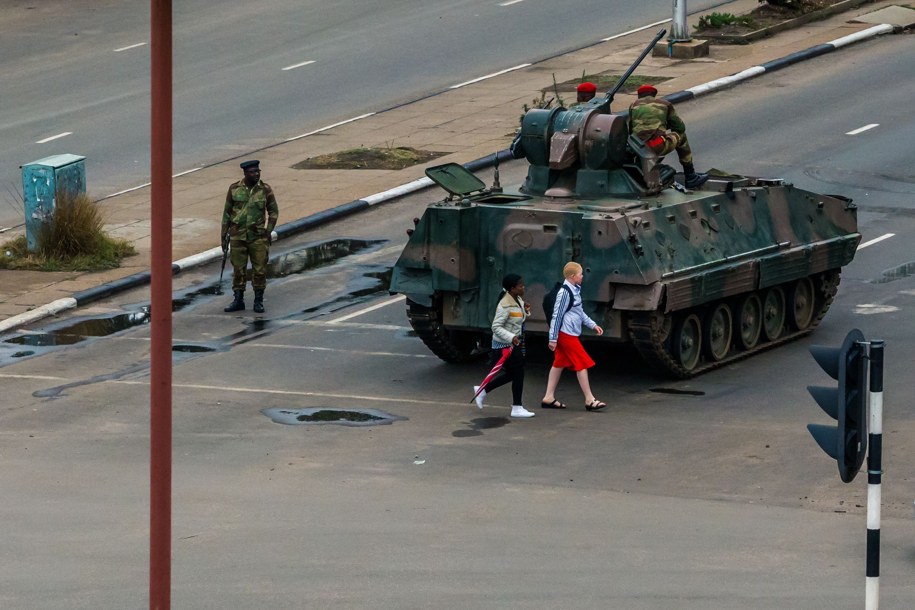 Two young women cross the street in Zimbabwe's capital, Harare, as soldiers regulate traffic at the intersection.
