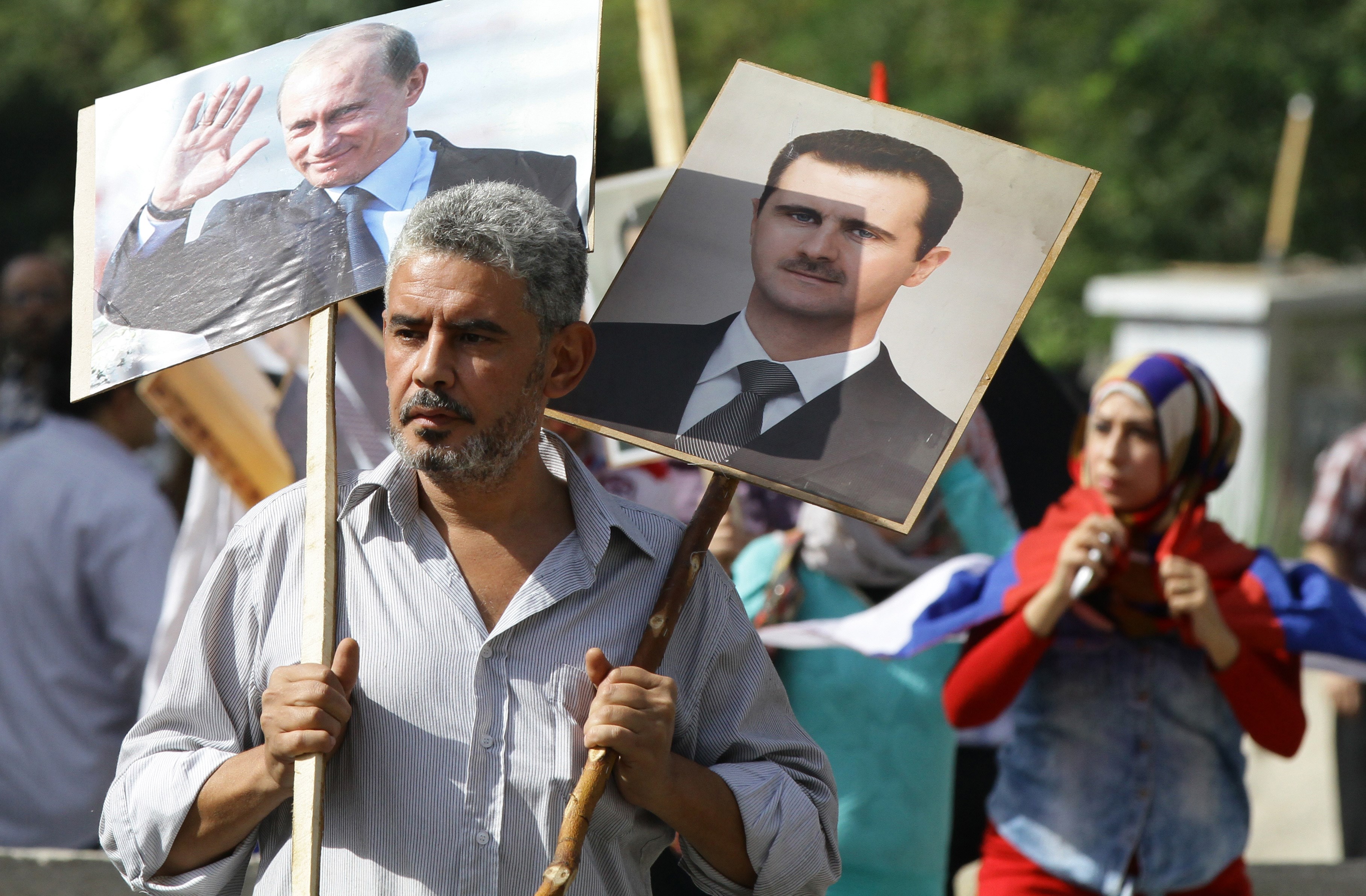 A Syrian man holds portraits of Syrian President Bashar al Assad and his Russian counterpart, Vladimir Putin.